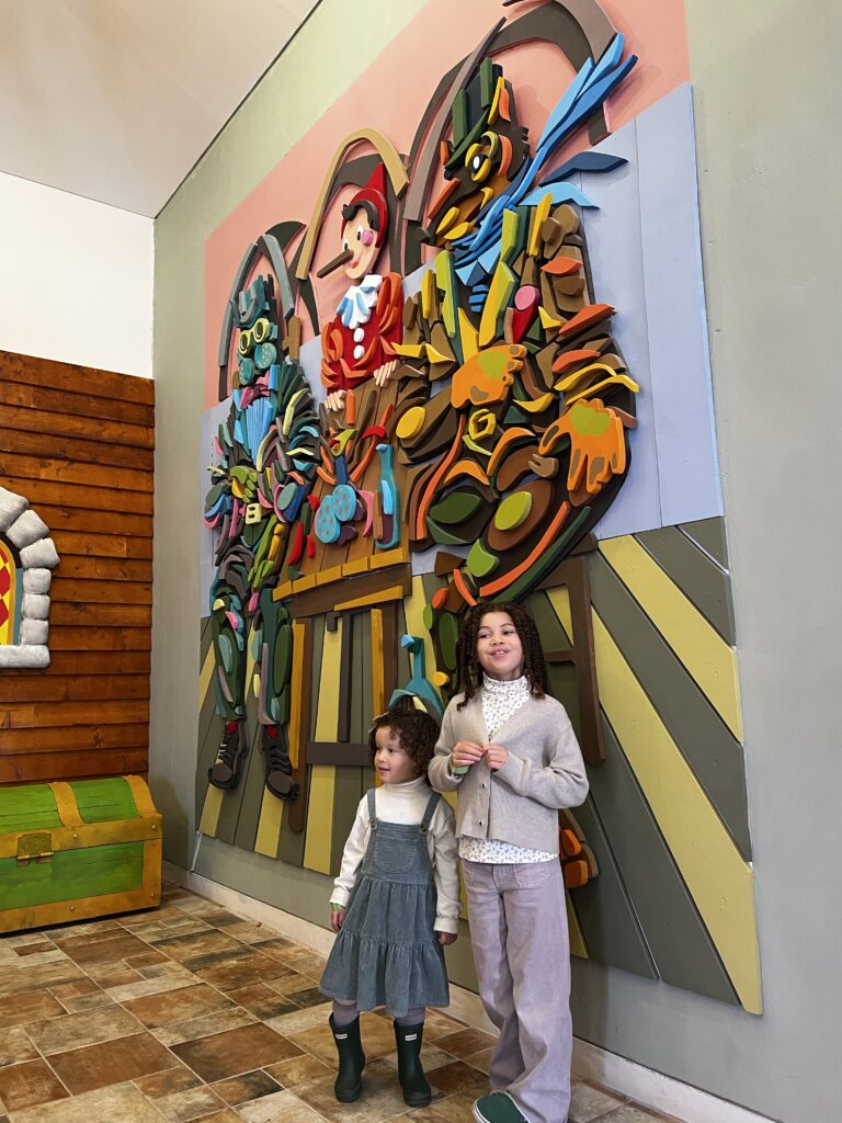 My daughters standing in front of the Pinocchio mural wall.